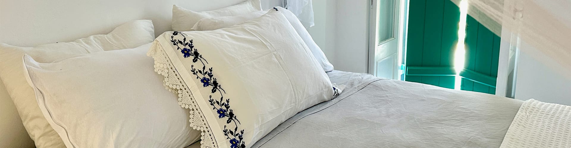 Luxurious Greek villa bedroom with traditional embroidered linens and turquoise shutters at Secret Greek Escape