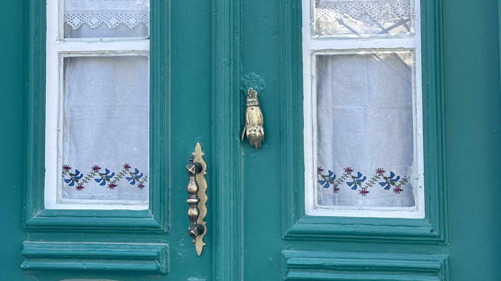 Traditional turquoise Greek villa door with brass knocker and embroidered curtains at Philoxenia Blue rental property