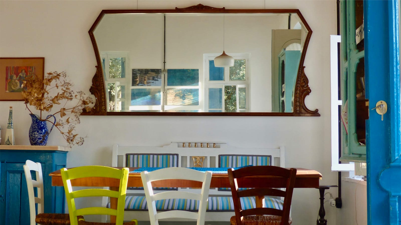 Traditional Greek villa kitchen with colorful wooden chairs, vintage mirror, and blue Mediterranean decor at Philoxenia Green rental villa